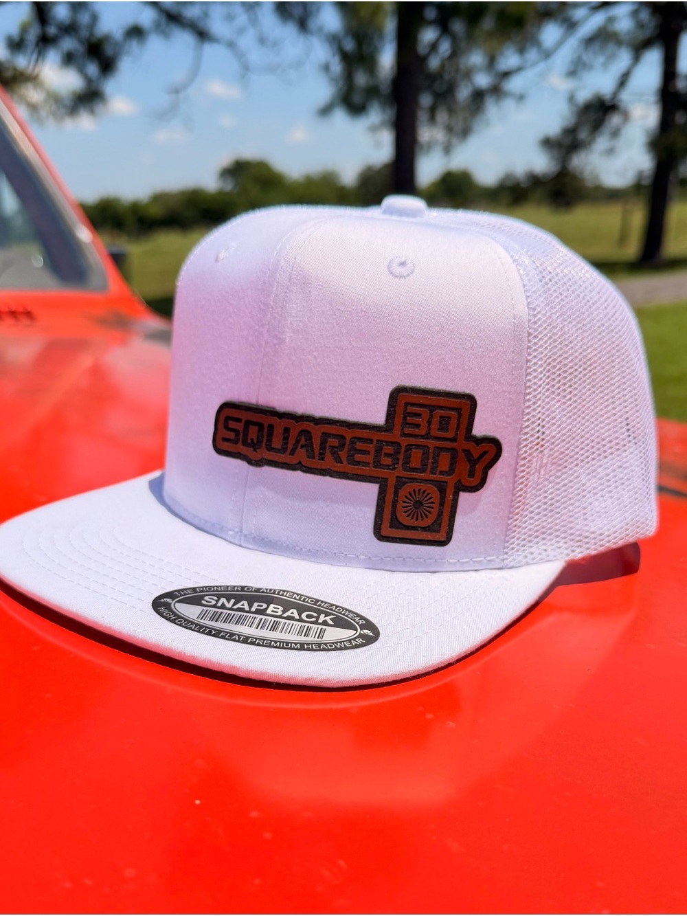 Unbranded white snapback flatbill hat with a squarebody leather patch.
